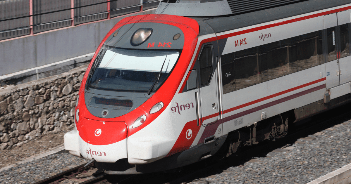 Fotografía en ángulo picado de un tren Renfe Cercanías de color blanco y rojo circulando por las vías cerca de una pared de piedra. Esta imagen ilustra la noticia sobre la denuncia de agresión tránsfoba ocurrida en la línea de Málaga a Torremolinos.