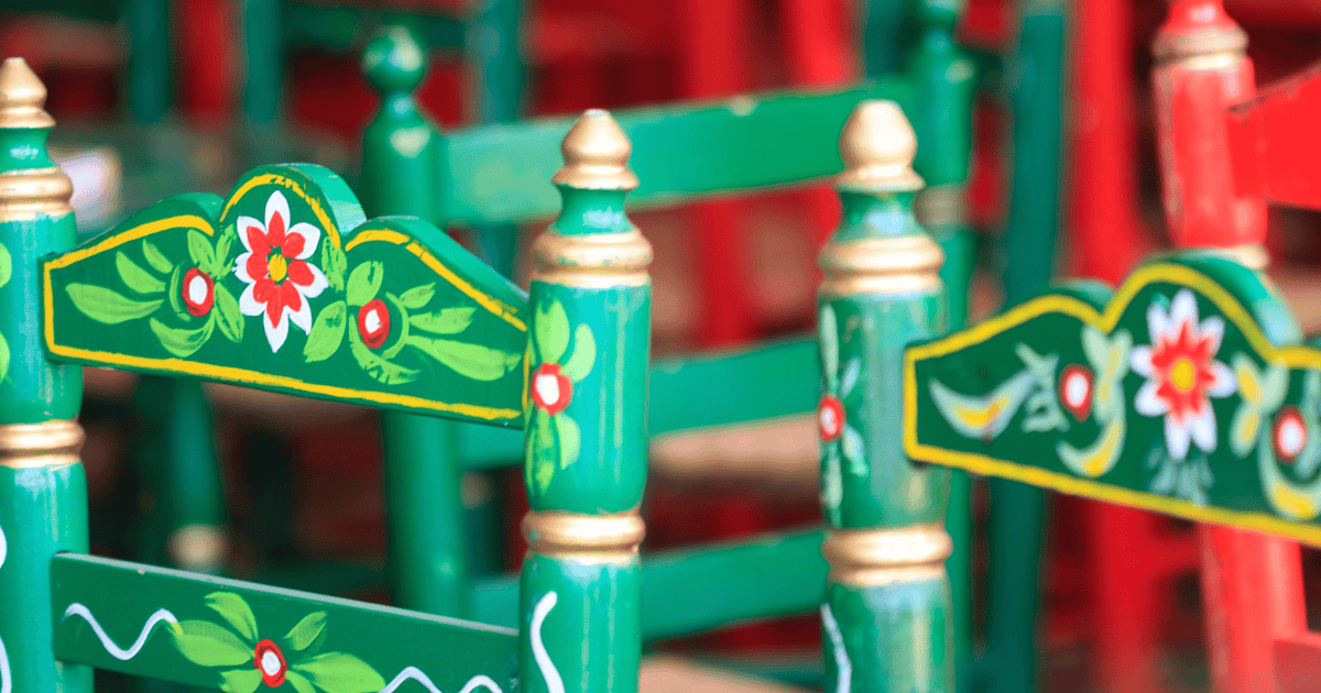 Primer plano de los respaldos de varias sillas de madera tradicionales de la Feria de Abril de Sevilla, pintadas de verde con detalles florales típicos en blanco y rojo.