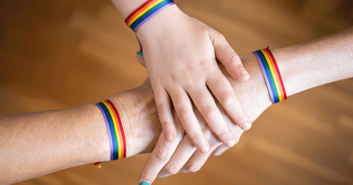 Plano cenital de tres manos unidas con pulseras arcoíris por el Día Mundial de la Prevención del suicidio en el colectivo LGTBIQA+.